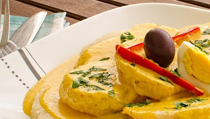 Plato blanco con papas con salsa huancaína, huevo duro y una aceituna coronando el plato.