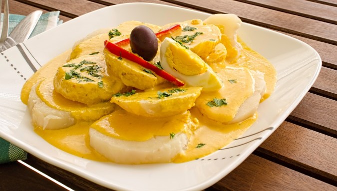 Plato blanco con papas con salsa huancaína, huevo duro y una aceituna coronando el plato.