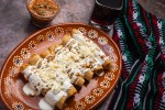 Plato de comida con flautas de papas, decorados con crema, lechuga y queso