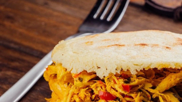 Arepa rellena de pollo desmechado sobre una tabla de madera