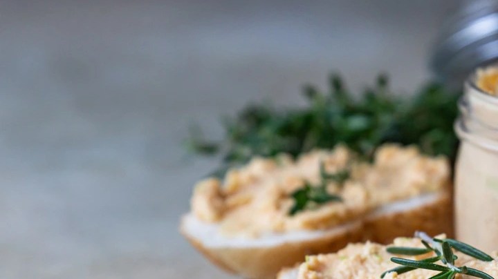 Frasco de vidrio con dip de diablitos con queso crema sobre una mesa de madera y pedazos de pan