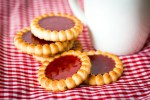 Galletas reinitas de mermelada de fresa sobre un mantel de cuadros rojos y una taza blanca