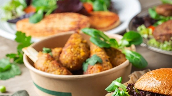 Mesa con mantel marrón con diferentes platos con hamburguesas de carne vegana y papas fritas