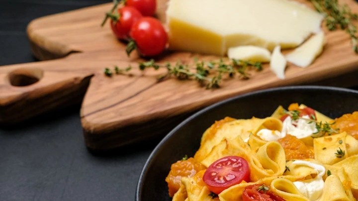 Plato negro con pappardelle con salsa de queso azul y calabaza en una mesa gris