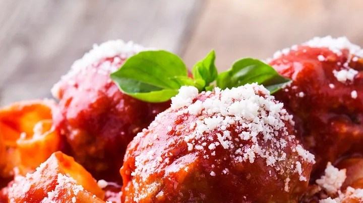 Plato negro con una porción de pappardelle con salsa de tomate y albóndigas sobre una pared de madera