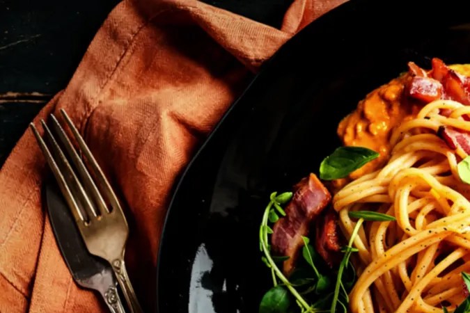 Plato negro con una cremosa pasta a la carbonara de calabaza