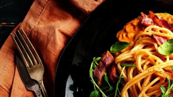 Plato negro con una cremosa pasta a la carbonara de calabaza