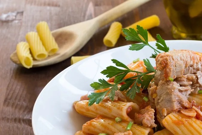 Plato blanco hondo con rigatoni con atún sobre una mesa de madera