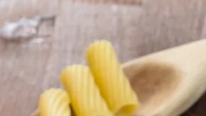 Plato blanco hondo con rigatoni con atún sobre una mesa de madera