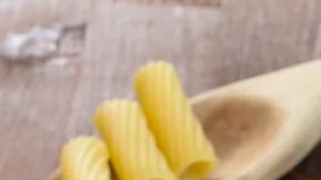 Plato blanco hondo con rigatoni con atún sobre una mesa de madera