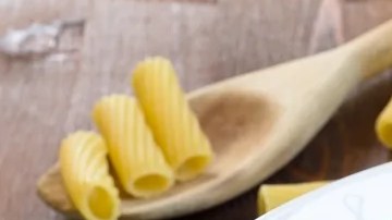 Plato blanco hondo con rigatoni con atún sobre una mesa de madera