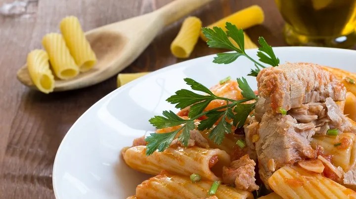 Plato blanco hondo con rigatoni con atún sobre una mesa de madera