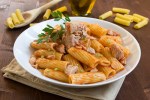 Plato blanco hondo con rigatoni con atún sobre una mesa de madera
