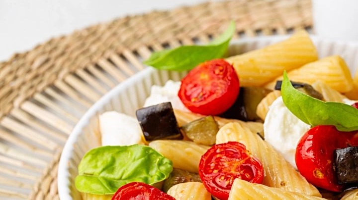 Plato blanco hondo con rigatoni con berenjena y mozzarella sobre una mesa marrón