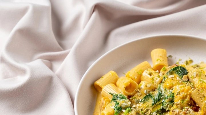 Plato blanco con pasta rigatoni con salsa de nueces sobre un mantel blanco