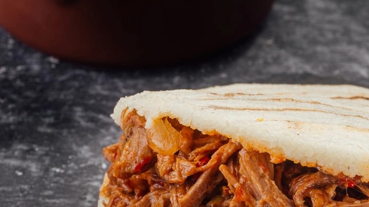 Una arepa rellena de carne mechada o desmechada sobre una mesa de color negro
