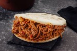 Una arepa rellena de carne mechada o desmechada sobre una mesa de color negro