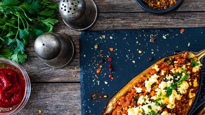 Berenjenas rellenas de carne, queso y verduras sobre un plato de aluminio, decorada con verduras