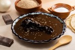 Plato hondo con mole negro sobre una mesa blanca decorado con ingredientes