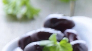 Envase de vidrio con paté de aceitunas negras sobre una tabla de madera y rodajas de pan