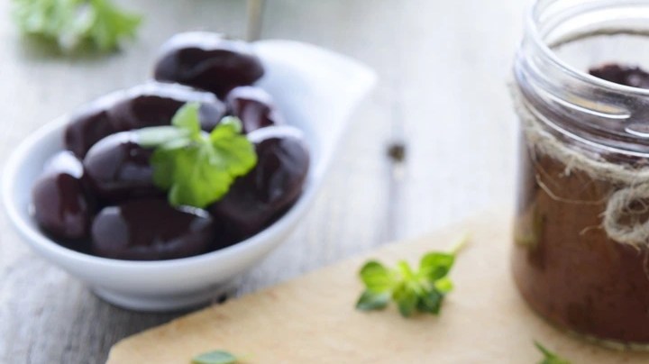 Envase de vidrio con paté de aceitunas negras sobre una tabla de madera y rodajas de pan