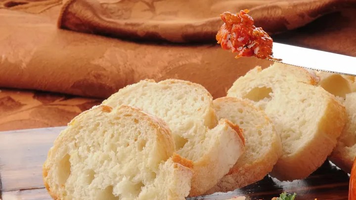 Tabla de madera con un frasco de vidrio con paté de pimientos de piquillo, untado en pedazos de pan