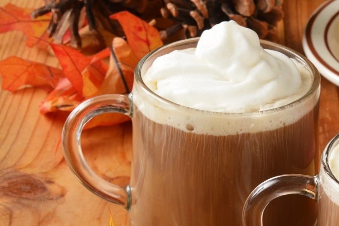 Tazas de café navideño decorado con crema batida sobre una mesa de madera