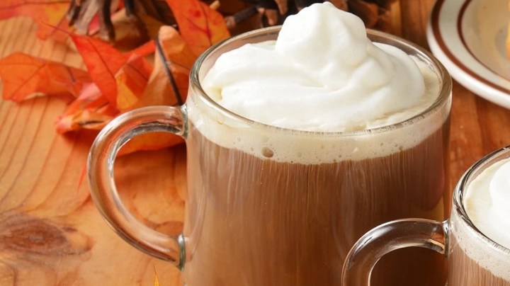 Tazas de café navideño decorado con crema batida sobre una mesa de madera