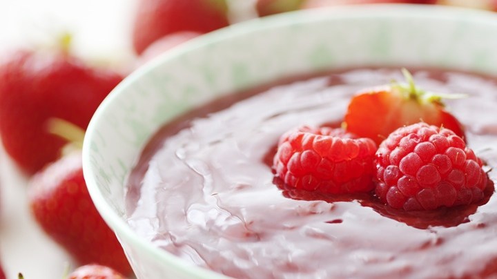 Porción de compota de frutos rojos en un recipiente blanco decorado con frutillas