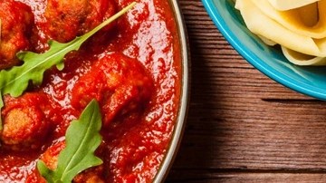 Plato azul con pasta pappardelle con salsa arrabbiata sobre una mesa de madera y manteles de cuadro