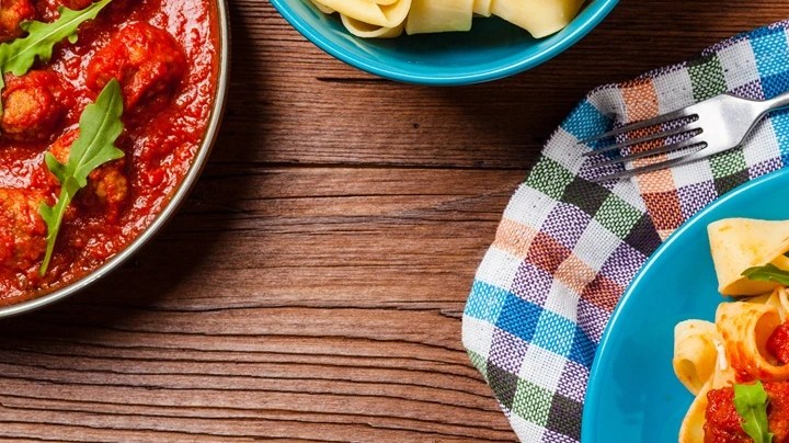 Plato azul con pasta pappardelle con salsa arrabbiata sobre una mesa de madera y manteles de cuadro