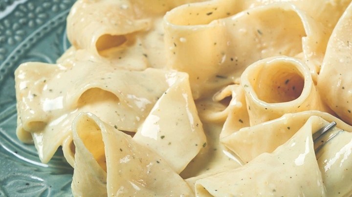 Pasta Pappardelle con salsa cremosa y parmesano sobre un plato verde y un tenedor