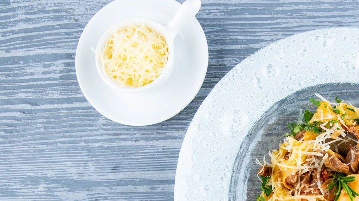 Pasta pappardelle con salsa de calabaza y tocino en un plato blanco sobre una mesa gris