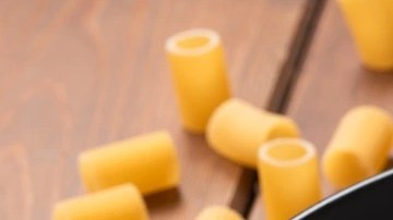 Rigatoni con espárragos en un plato negro sobre una mesa de madera