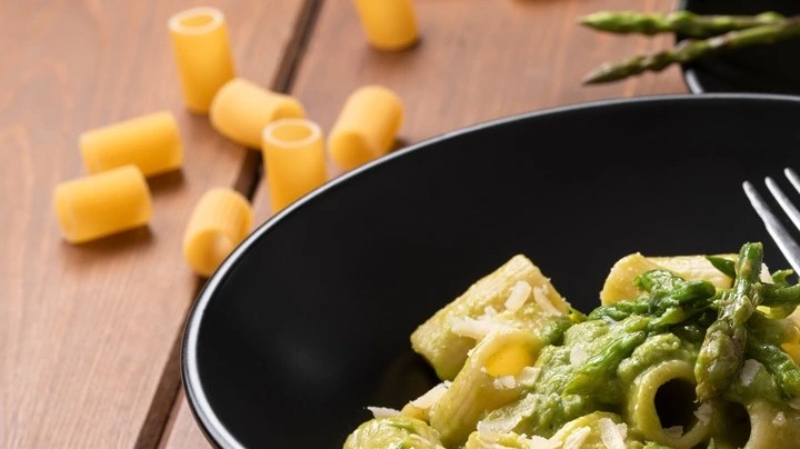 Rigatoni con espárragos en un plato negro sobre una mesa de madera