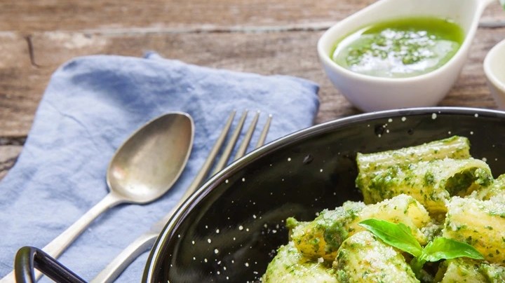 Olla negra con rigatoni con pesto sobre una mesa de madera decorado con cubiertos