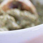 Salsa de mole amarillo servida en un tazón blanco con una cuchara de madera, sobre un mantel tradicional mexicano