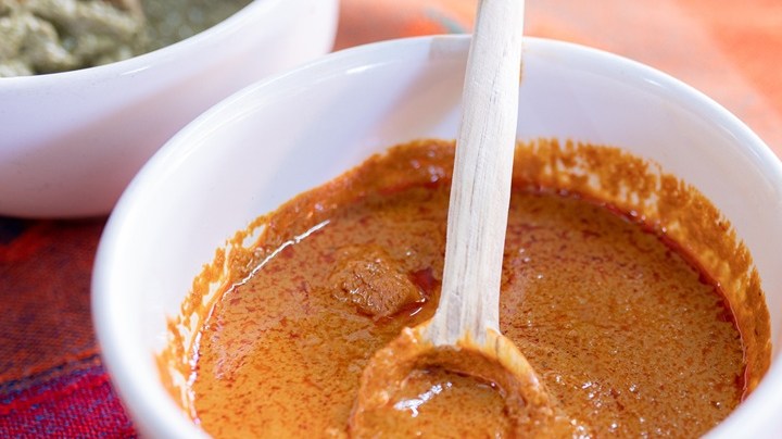 Salsa de mole amarillo servida en un tazón blanco con una cuchara de madera, sobre un mantel tradicional mexicano