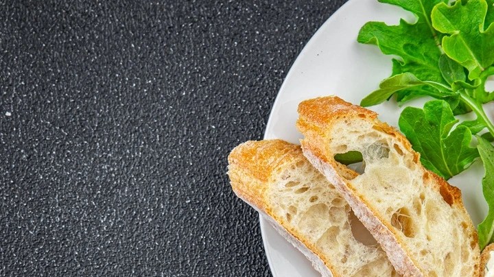 Paté de cangrejo servido sobre pan artesanal crujiente acompañado de hojas verdes frescas en un plato blanco.