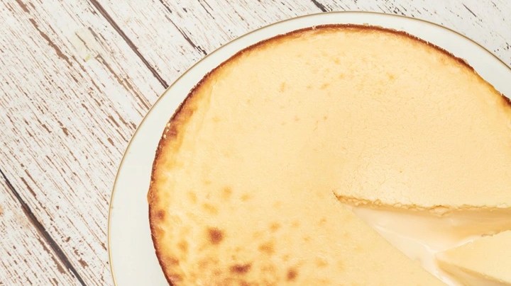 Plato blanco con una cheesecake de yogur griego cortada por pedazos sobre una mesa de madera