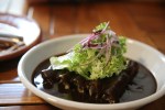 Plato blanco hondo con enmoladas de mole negro decoradas con una ensalada de aguacate