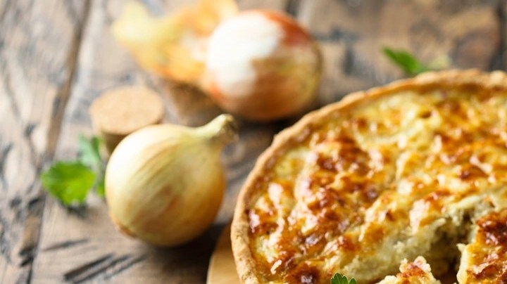 Quiche de cebolla caramelizada, pera y romero de forma redonda sobre una tabla de madera