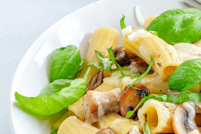 Plato blanco hondo con rigatoni con pollo y hongos