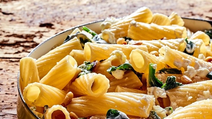 Sartén con rigatoni con ricotta y espinacas sobre una mesa de madera