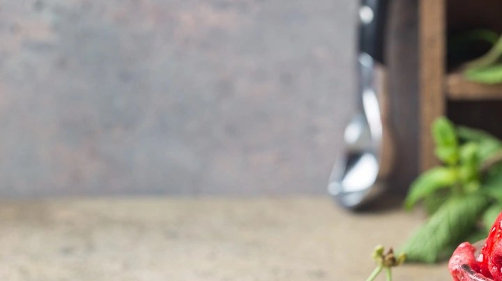 Una copa de vidrio con bolas de sorbete de cereza sobre una tabla de madera con decoraciones de hoja de menta