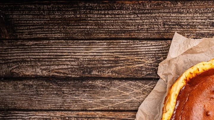 Un pedazo de tarta de queso gallega completa sobre una mesa de madera