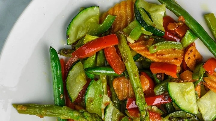 Plato blanco sobre una mesa de madera con vegetales salteados