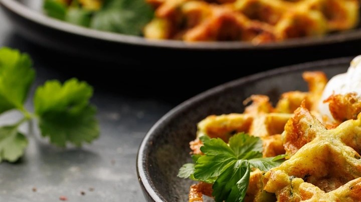 Waffle de calabacín y queso sobre un plato negro decorado con crema y perejil