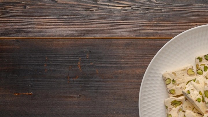 Plato blanco con pedazos de turrón de pistachos sobre una mesa de madera
