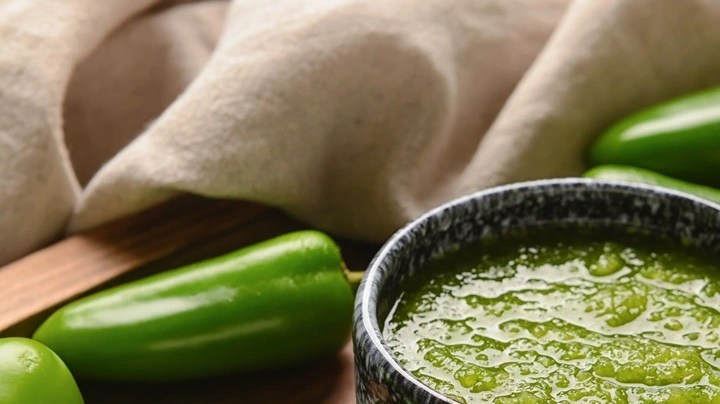 Una taza gris con adobo de chile verde sobre una mesa decorada con chiles verdes